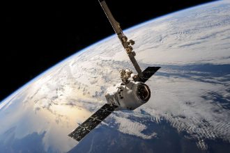 Satélite sobrevoa a Terra, com nuvens e o espaço ao fundo.