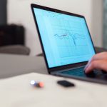 Pessoa analisando um gráfico de dados em um laptop, em um contexto de monitoramento e pesquisa.