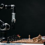 Braço robótico movimenta uma peça em um tabuleiro de xadrez, em uma demonstração de inteligência artificial e automação.