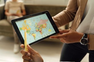 Mãos seguram um tablet que exibe um mapa-múndi, representando o uso de tecnologia digital na educação em escala global.