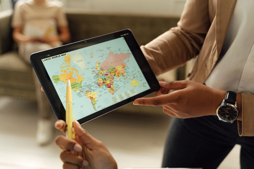Mãos seguram um tablet que exibe um mapa-múndi, representando o uso de tecnologia digital na educação em escala global.