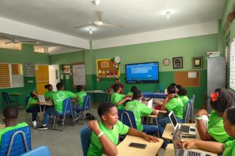 Grupo de estudantes reunido em sala de aula, usando laptops durante uma atividade acadêmica.