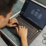 Profissional de óculos trabalha em um laptop com uma interface de inteligência artificial aberta na tela.