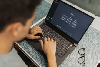 Profissional de óculos trabalha em um laptop com uma interface de inteligência artificial aberta na tela.