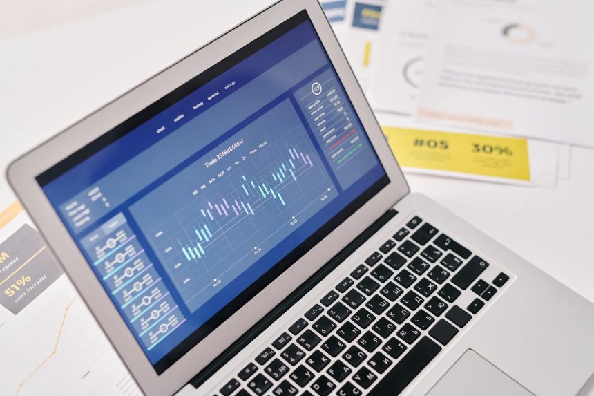 Laptop exibindo gráficos e análises financeiras sobre uma mesa, cercado por documentos.