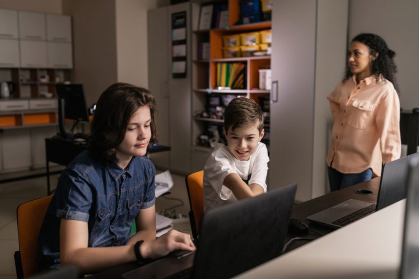 Professor supervisiona estudantes que usam computadores portáteis em uma sala de aula moderna.