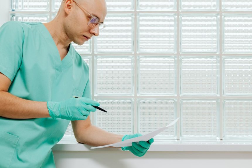 Profissional da saúde, usando luvas e roupa hospitalar, examina atentamente um documento.