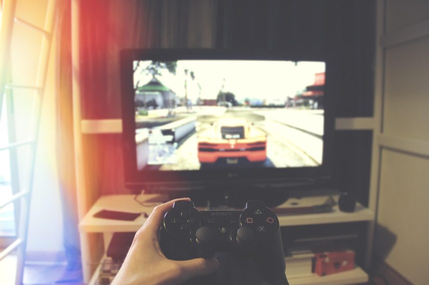 Mão segurando um controle de videogame diante de uma televisão.